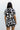 Upper body back view of female model wearing the Valerie Black & White Short Sleeve Romper that has a black and white abstract print, short sleeves, a collar, button up front, and elastic waist with tie.