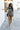 Full body front view of female model wearing the Valerie Black & White Short Sleeve Romper that has a black and white abstract print, short sleeves, a collar, button up front, and elastic waist with tie.