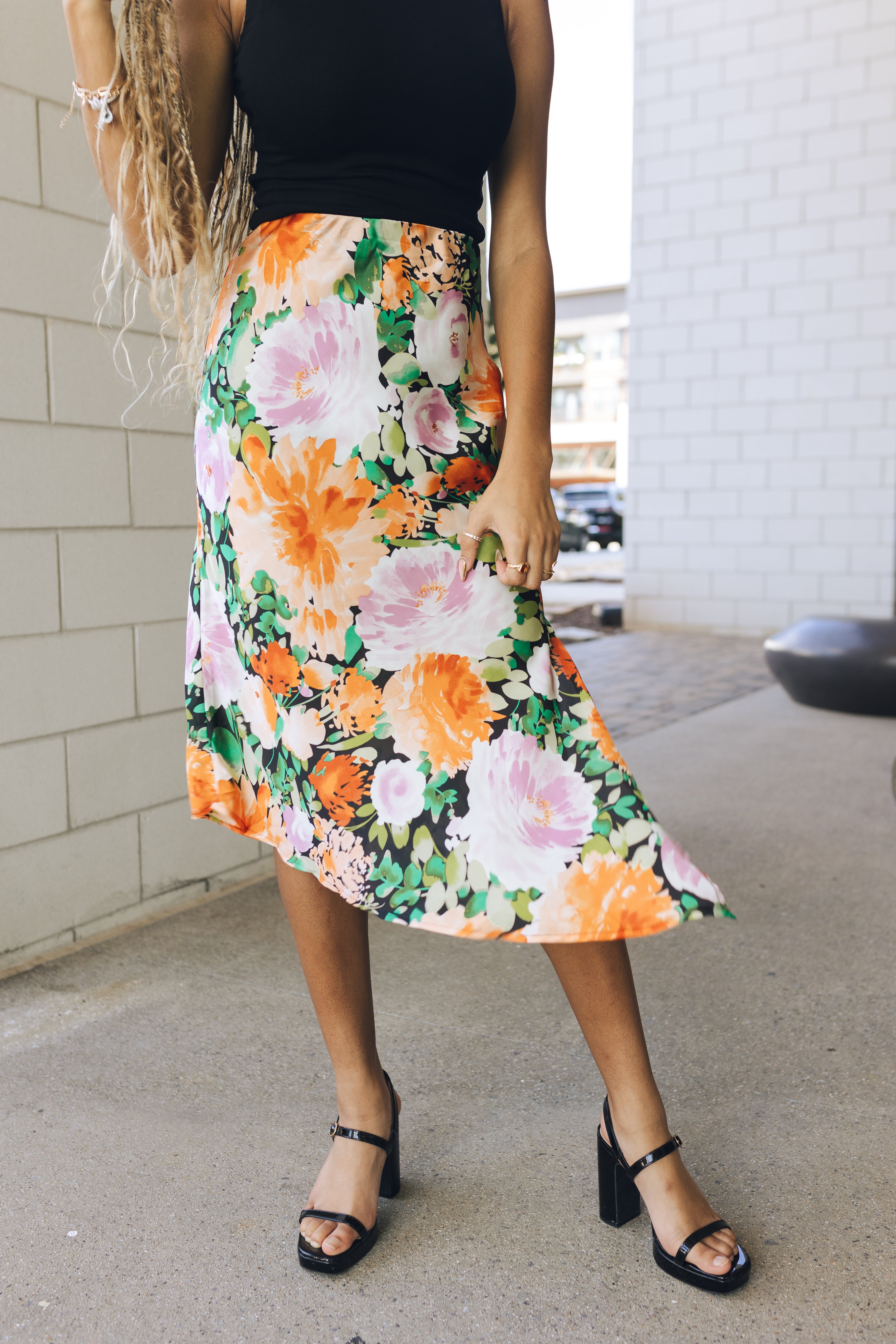 Close up view of model wearing the Amalia Black Floral Midi Skirt. This is a black midi skirt with multicolored floral pattern, satin.