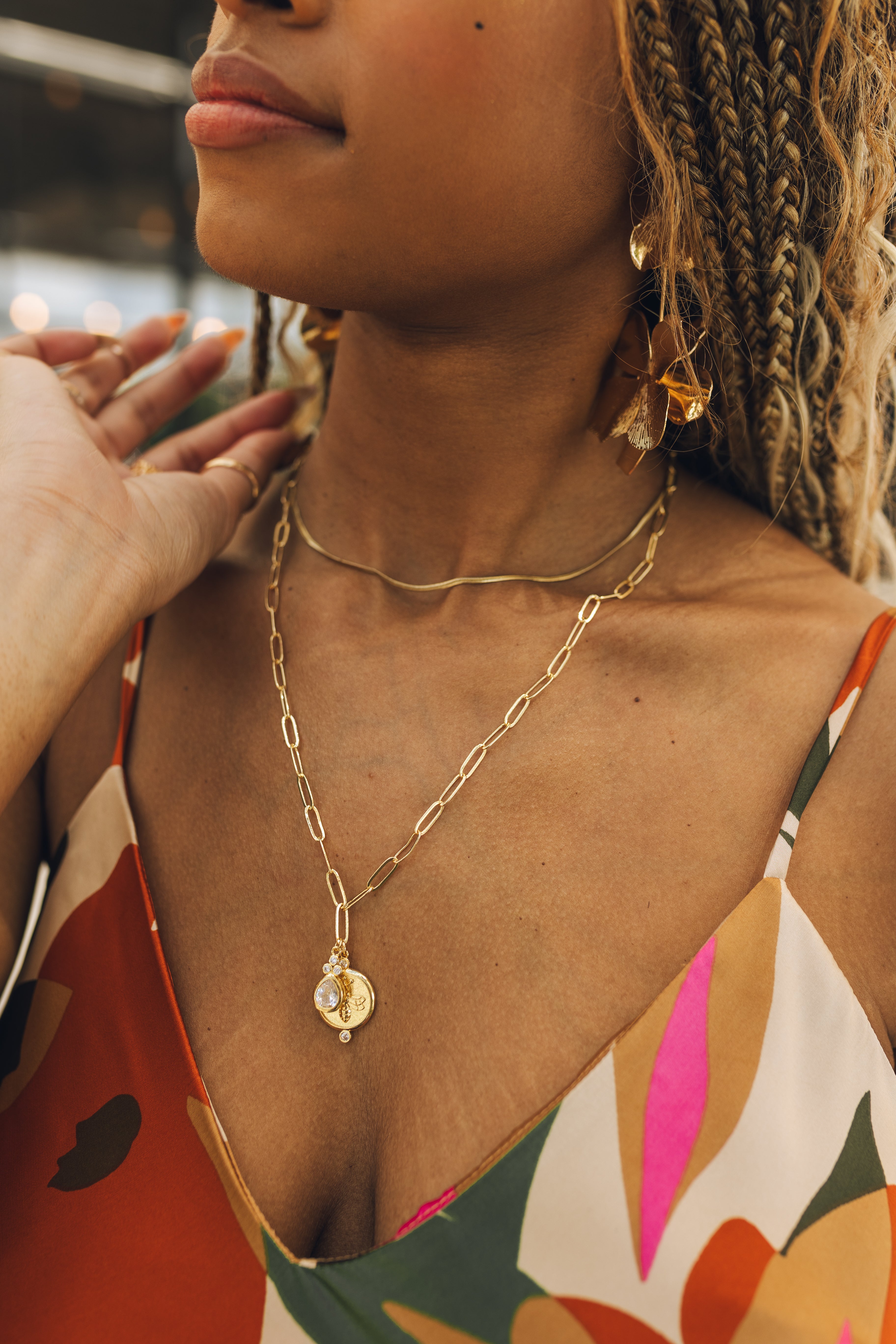 Close up of model wearing the Gianna Gold Pendant Necklace. This is a gold chain necklace with circular bee medallion and clear rhinestone teardrop.