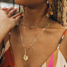 Close up of model wearing the Gianna Gold Pendant Necklace. This is a gold chain necklace with circular bee medallion and clear rhinestone teardrop.