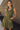 Close up view of model wearing the Holly Olive Mini Dress. This is a green mini dress with a zipper up the front and ruffled bottom, V neckline, sleeveless.