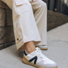 Close-up side view of female model wearing the Vesta Sneakers in White & Black with beige pants.