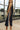 Close up of model wearing the Lillian Black Midi Dress. This is a black sleeveless midi dress with rust and cream wavy trim on sides, slit on bottom.