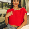 Close up of model wearing the Kendra Knit Crop Top. This top is cropped and knit, options of either orange or red for purchase. Round neckline and white trim, sleeveless