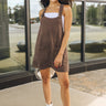 Full body view of model wearing the Lacey Oak Denim Mini Dress. This is a oak colored denim mini dress, with two pockets on the front, sleeveless.