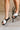 Side view of female model wearing the VIIBE CrissCross Slide Flat Sandal in Black & Sea Salt which features Black and White Leather Crisscross Straps, Sporty Slide-On Style, Scalloped Sole and Round Toe