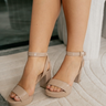 Right front angle view of female model wearing the Go On 2 Dress Sandal which features nude patent leather fabric, monochrome block heel, a delicate adjustable ankle strap, and a narrow vamp.