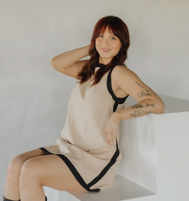 image of woman sitting on steps in a beige and black trim dress