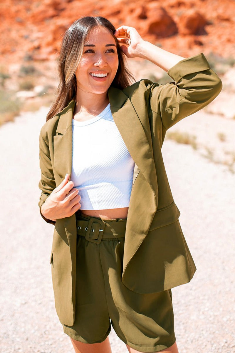 Frontal view of the Livin' The Dream Shorts that features an olive green colored material, a high-rise fit, an elastic waist, a belt detail, side pockets, and a flowy fit. Worn with matching blazer