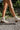 Model wearing the Untie Ankle Boot that features a white PU material, a traditional western boot silhouette, a shortened shaft, western inspired embroidery, a zipper closure, and a stacked 2" heel.