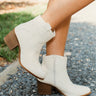 Model wearing the Untie Ankle Boot that features a white PU material, a traditional western boot silhouette, a shortened shaft, western inspired embroidery, a zipper closure, and a stacked 2" heel.