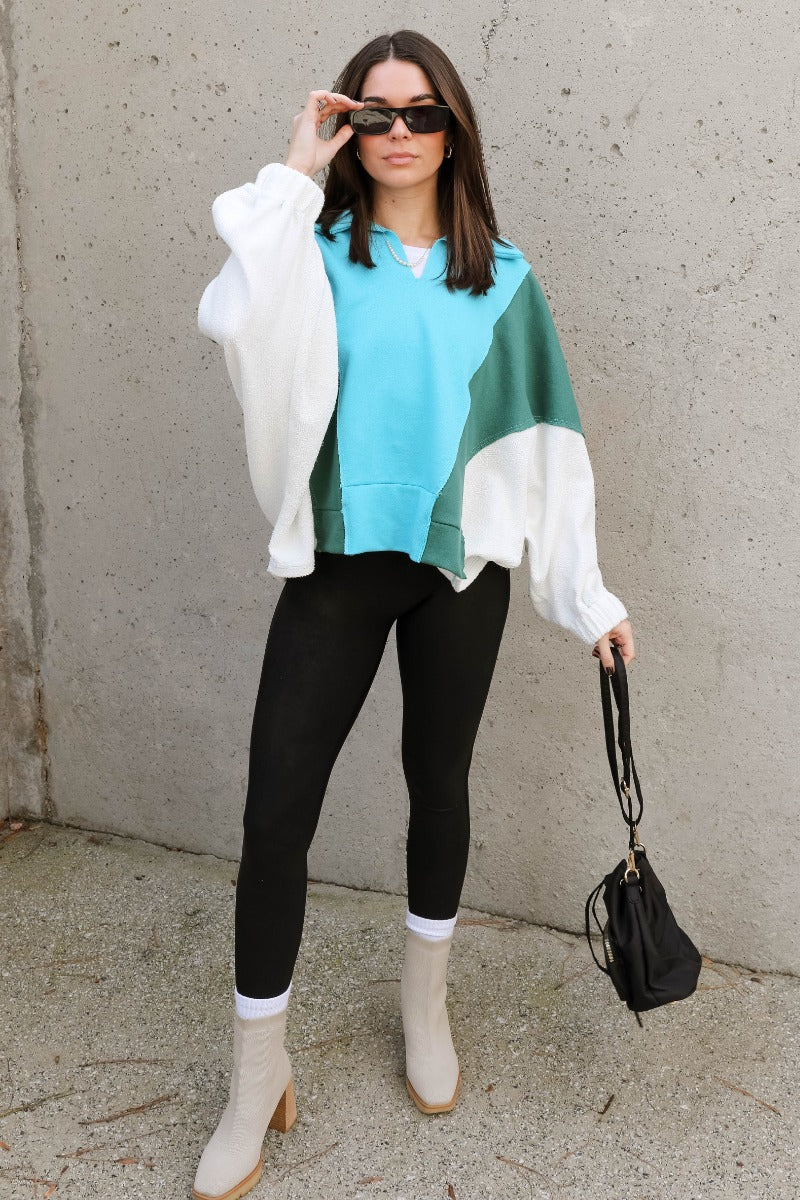 Full body view of model wearing the Ashley Blue Multi Color Block Sweatshirt which features blue, green and white knit fabric, a color block pattern, textured details, a collared neckline with a v-cutout, and long sleeves with elastic cuffs.