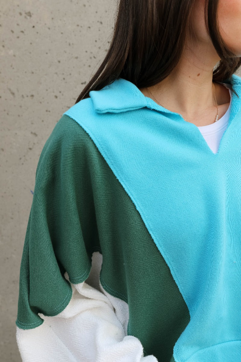 Close up view of model wearing the Ashley Blue Multi Color Block Sweatshirt which features blue, green and white knit fabric, a color block pattern, textured details, a collared neckline with a v-cutout, and long sleeves with elastic cuffs.
