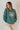 front view of model wearing the Lake Tahoe Green Embroidered Sweatshirt that has heather teal green fabric, a round neckline, dropped shoulders, and long sleeves with cuffs. 