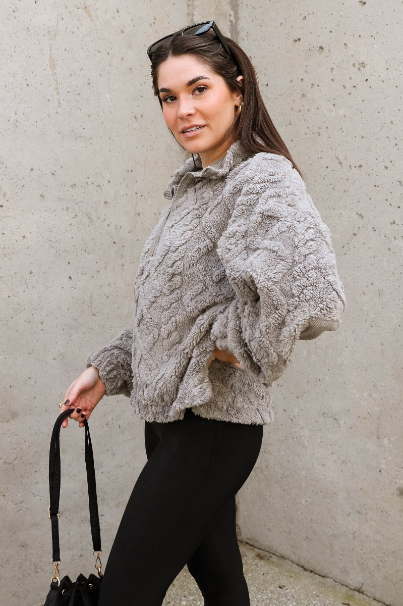 Side view of model wearing the Layla Grey Quarter Zip-Up Pullover which features soft grey textured fabric with a monochrome geometric pattern, an elastic band, a monochrome quarter zip-up, dropped shoulders, and long balloon sleeves with elastic cuffs.