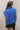 Back view of model wearing the Noelle Blue Cable Knit Sleeveless Sweater which features blue cable knit fabric, ribbed hem, high neckline and sleeveless.