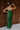 Full body back view of model wearing the Noelle Hunter Green Velvet Ribbed Strapless Midi Dress which features moss green velvet ribbed fabric, slit on the side, maxi length and strapless.