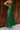 Full body side view of model wearing the Noelle Hunter Green Velvet Ribbed Strapless Midi Dress which features moss green velvet ribbed fabric, slit on the side, maxi length and strapless.