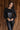 front view of model wearing the Lyra Black Sequin Long Sleeve Top that has black sequin fabric, black lining, a cropped waist, a round neckline, a back zipper, and long sleeves.