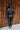Full body back view of model wearing the Lyra Black Sequin Long Sleeve Top that has black sequin fabric, black lining, a cropped waist, a round neckline, a back zipper, and long sleeves.