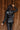 Back view of model wearing the Lyra Black Sequin Long Sleeve Top that has black sequin fabric, black lining, a cropped waist, a round neckline, a back zipper, and long sleeves.