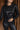 Close front view of model wearing the Lyra Black Sequin Long Sleeve Top that has black sequin fabric, black lining, a cropped waist, a round neckline, a back zipper, and long sleeves.