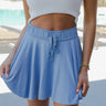 Front view of model wearing the Sunny Skies Skort that has dusty blue lightweight fabric, an elastic waist with drawstring ties, fitted dusty blue shorts, and a skirt overlay with slits on each side