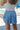 Back view of model wearing the Sunny Skies Skort that has dusty blue lightweight fabric, an elastic waist with drawstring ties, fitted dusty blue shorts, and a skirt overlay with slits on each side