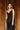 Upper front view of model wearing the Colette Black Floral Satin Midi Dress that has black satin fabric, monochrome florals, a assymetrical ruffle tier design, pleated fabric, a cowl neck, and thin straps.