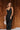 Full body front view of model wearing the Colette Black Floral Satin Midi Dress that has black satin fabric, monochrome florals, a assymetrical ruffle tier design, pleated fabric, a cowl neck, and thin straps.