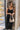 front view of model wearing the Colette Black Floral Satin Midi Dress that has black satin fabric, monochrome florals, a assymetrical ruffle tier design, pleated fabric, a cowl neck, and thin straps.