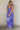 Full body view of model wearing the Harlow Blue & Purple Floral Ruffle Midi Dress which features blue and purple sheer fabric, floral print, light purple metallic, blue lining, three tiered skirt, midi length, plunge neckline, adjustable ruffle straps, op