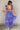 Full body back view of model wearing the Harlow Blue & Purple Floral Ruffle Midi Dress which features blue and purple sheer fabric, floral print, light purple metallic, blue lining, three tiered skirt, midi length, plunge neckline, adjustable ruffle strap