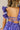 Close up back view of model wearing the Harlow Blue & Purple Floral Ruffle Midi Dress which features blue and purple sheer fabric, floral print, light purple metallic, blue lining, three tiered skirt, midi length, plunge neckline, adjustable ruffle straps