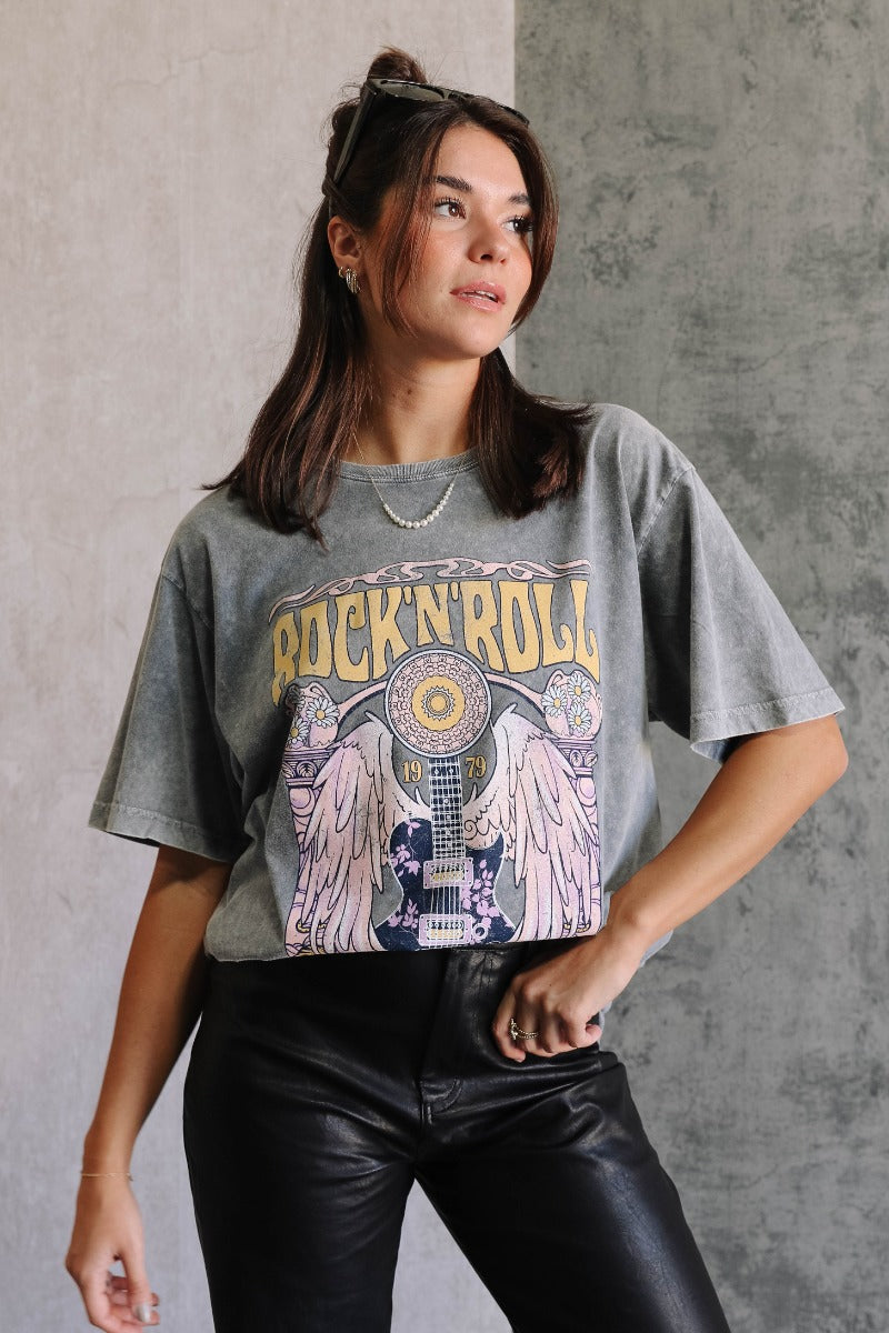 Front view of model wearing the Rock 'N' Roll Washed Short Sleeve Graphic Tee that has washed cotton fabric, a round neck and short sleeves. Graphic says "Rock N' Roll, World Tour" with a guitar and angel wings.