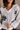 Close up view of model wearing the Daisy Floral Navy & Cream Long Sleeve Hoodie Sweater which features cream knit fabric with a yellow and navy blue floral print, a high-low thick ribbed hem, a v-neckline with a hood and tie closure, dropped shoulders, an