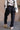 Back view of model wearing the Ayla Washed Black Cargo Adjustable Jogger Pants which features washed black ribbed fabric, two front pockets, elastic waistband with drawstring tie, two side cargo pockets with tortoise button and wide pant legs with drawstr
