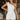 Front view of model wearing the All My Love Ruffle Romper which features white fabric, pockets on each side, a tie around the waist, one shoulder ruffle strap, and a monochromatic side zipper with a hook closure.