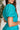 Close upper side view of model wearing the All For You Dress that has teal fabric with a lace floral pattern, mini length, teal lining, a tie around the waist, a surplice neckline, and short puff sleeves with elastic trim