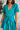 Close front view of model wearing the All For You Dress that has teal fabric with a lace floral pattern, mini length, teal lining, a tie around the waist, a surplice neckline, and short puff sleeves with elastic trim