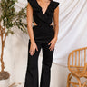 Front view of model wearing the She's All That Denim Jumpsuit that has black denim fabric, cutout details, a surplice neck with ruffles, a sleeveless design, flare pant legs, and a back zipper.