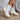 The Alexandra Boot is a white faux leather boot featuring a rounded toe, a stacked 1" platform, a stacked 2 1/2" heel, and a side zipper closure.