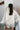 Back view of model wearing the Uptown Girl Sweater, that has an ivory knit fabric, a collared neck, long sleeves, a 3/4 button-up, and pearl and gold buttons. 