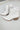 Side view of the Untie Ankle Boot that features a white PU material, a traditional western boot silhouette, a shortened shaft, western inspired embroidery, a zipper closure, and a stacked 2" heel.