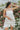 Frontal view of the Fields Of Dreams Dress that features an ivory satin material, an embroidered floral design, a straight neckline, a sleeveless design with thin adjustable straps, and a back zipper closure.