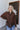 Front view of model wearing the Upstate Open-Back Top in Brown, which has textured brown fabric, a button-up front with a collar neckline, long sleeves, and a twist in the back with an open slit.