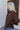 Side view of model wearing the Upstate Open-Back Top in Brown, which has textured brown fabric, a button-up front with a collar neckline, long sleeves, and a twist in the back with an open slit.