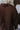 Close-up back view of model wearing the Upstate Open-Back Top in Brown, which has textured brown fabric, a button-up front with a collar neckline, long sleeves, and a twist in the back with an open slit.