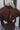 Close-up back view of model wearing the Upstate Open-Back Top in Brown, which has textured brown fabric, a button-up front with a collar neckline, long sleeves, and a twist in the back with an open slit.